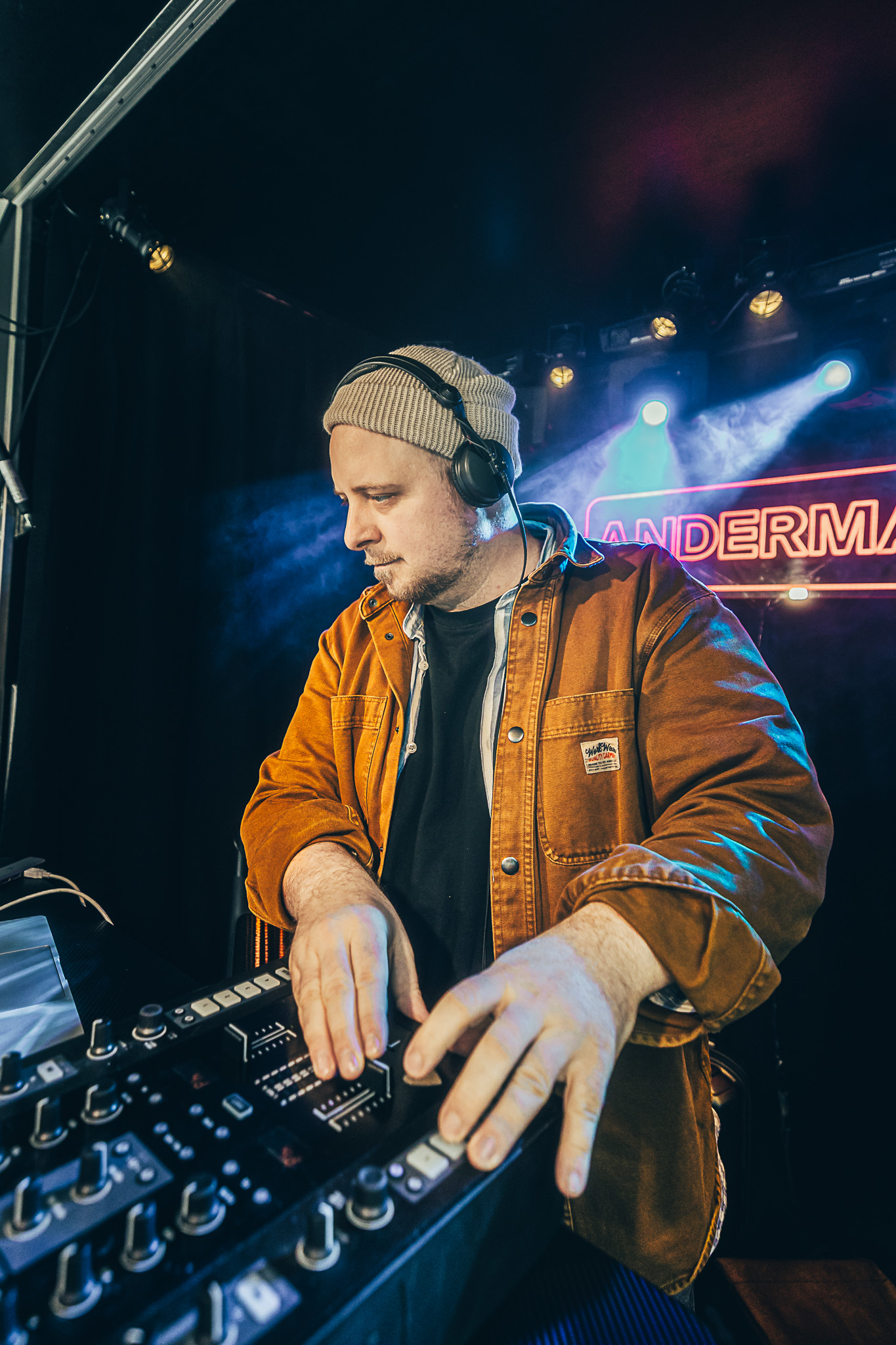 Simon alias DJ EISMANN mit Kopfhörern und Mütze am Mischpult, im Hintergrund Bühnenlicht.